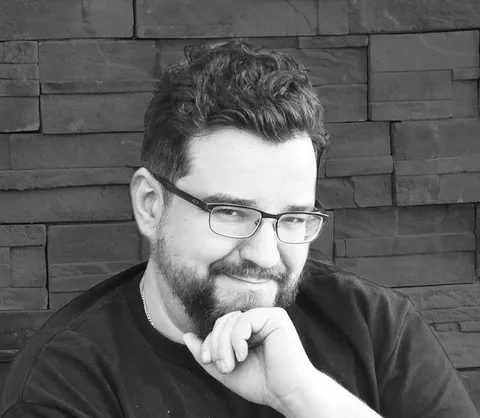 A black and white photo of a Caucasian man with wire-frame glasses and a goatee