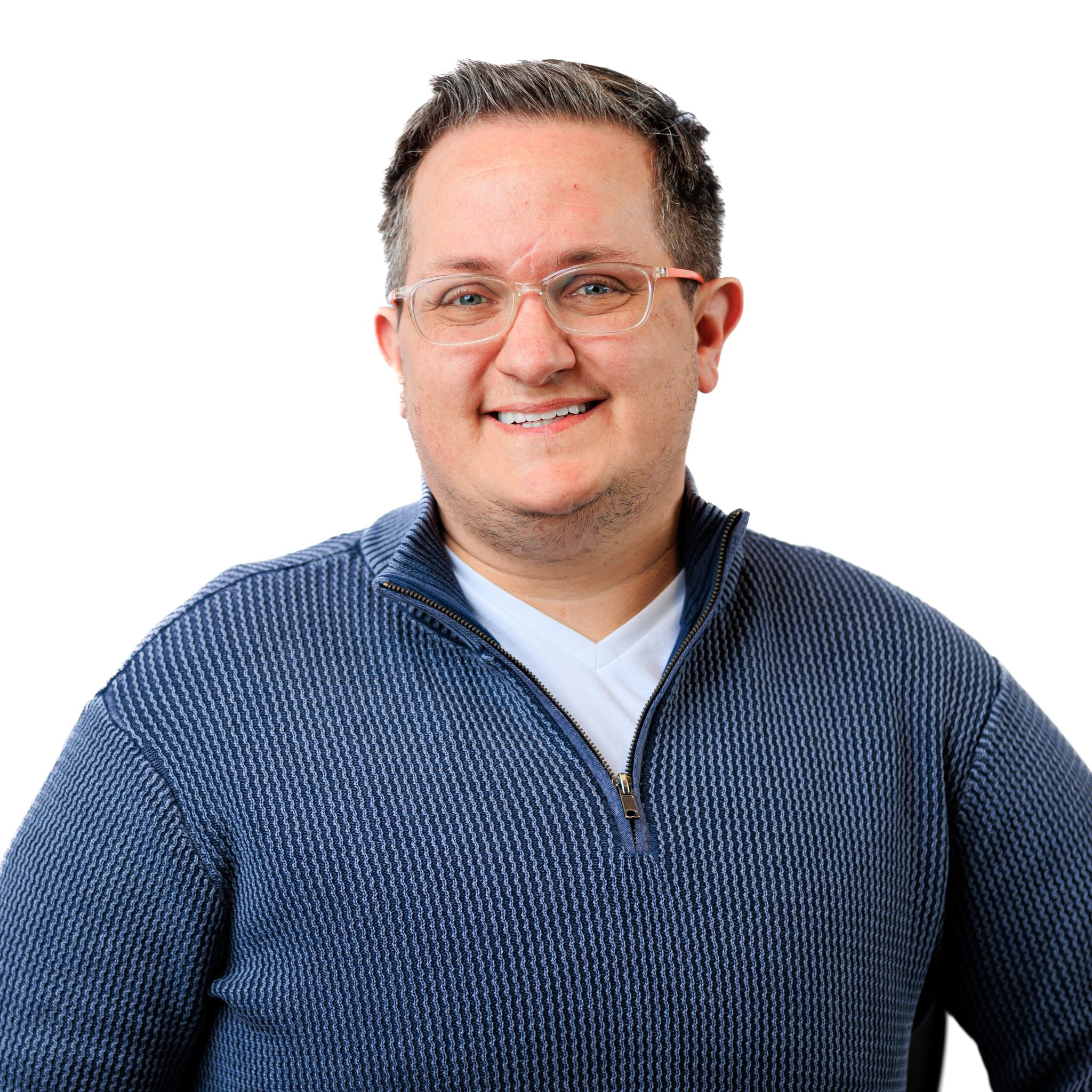 a smiling non-binary Caucasian person with clear-frame glasses and short, dark hair wearing a blue Henley