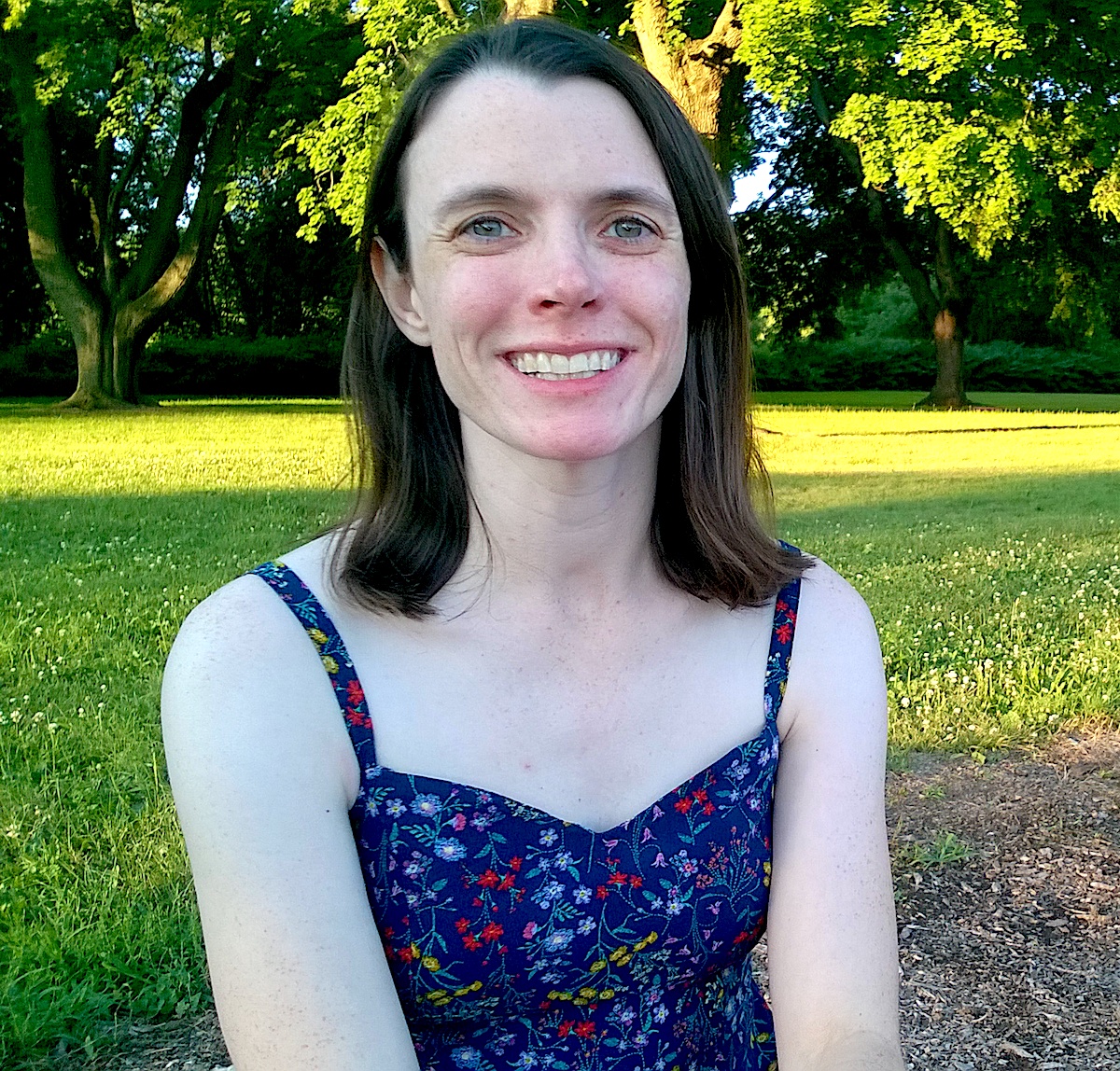 a smiling Caucasian woman with dark hair wearing a dark blue tanktop covered in blue flowers